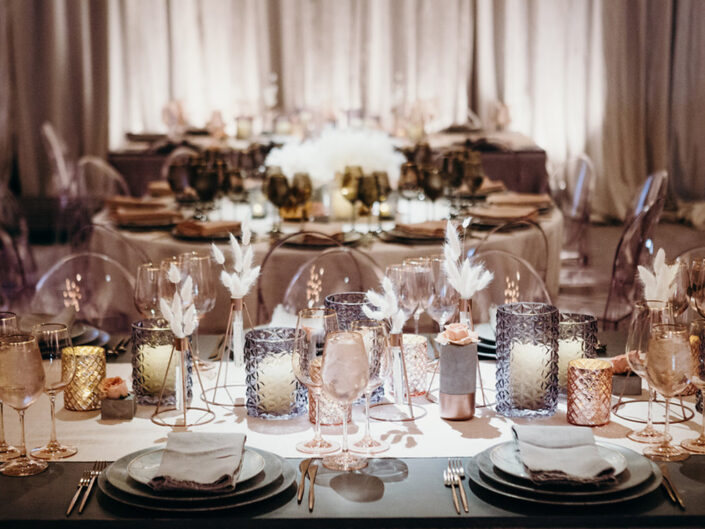 A table with blush metallic lurex linen, acrylic ghost chairs, pink votives, gray plates, and gold flatware.