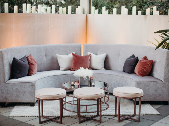Light gray banquette with black, coral, and white accent pillows and stools, creating a chic cocktail hour lounge