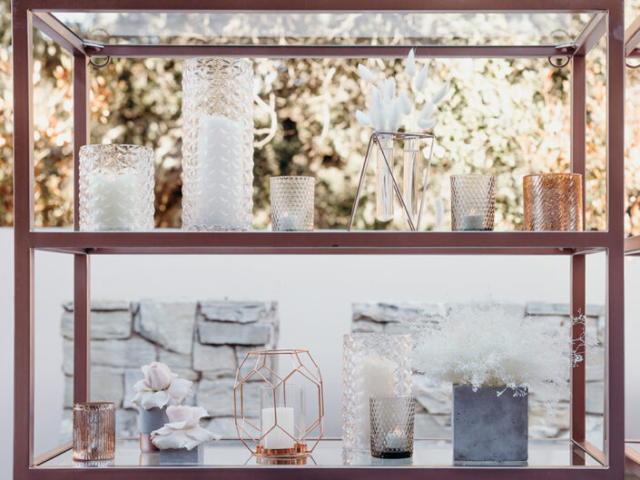 A rose gold metallic back bar adorned with candle votives, white amaranthus, and bunny tail flowers.